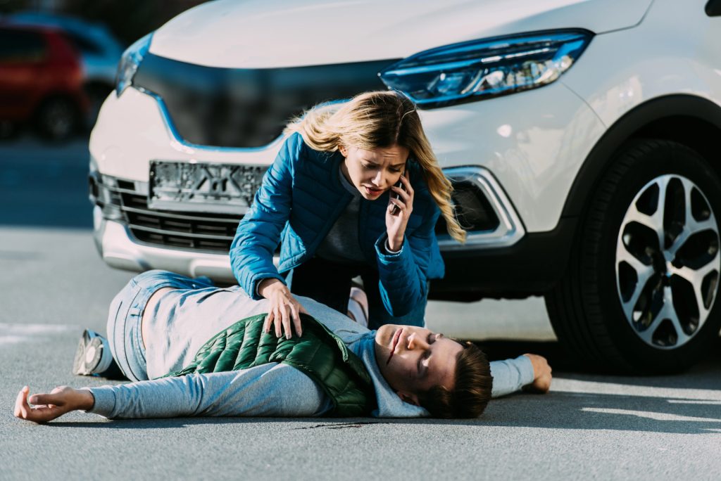 Woman kneels beside an injured man on the road while calling for help in front of an SUV