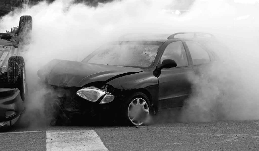 Damaged car surrounded by heavy smoke after a crash beside an overturned vehicle
